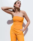 Femme portant un ensemble bustier moderne orange et pantalon large, mettant en valeur le top bandeau femme, parfait pour un look estival.