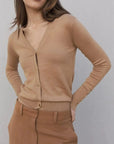 Femme portant un gilet tricot femme beige avec boutons, associé à un pantalon marron, illustration du style élégant et confortable.