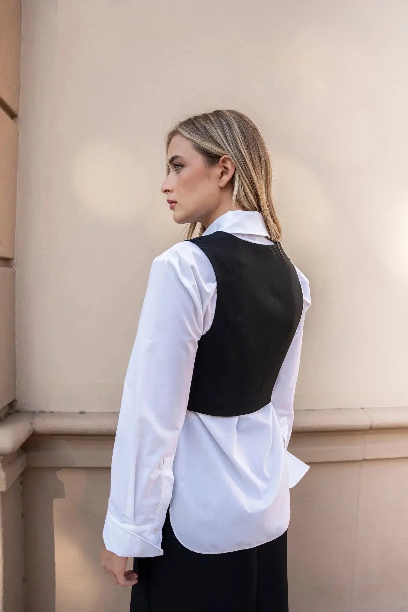 Femme en gilet court et pantalon large noir tenant un sac noir pour une touche tendance