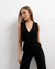 Femme posant en gilet costume femme court, associée à un pantalon noir pour une allure trendy.
