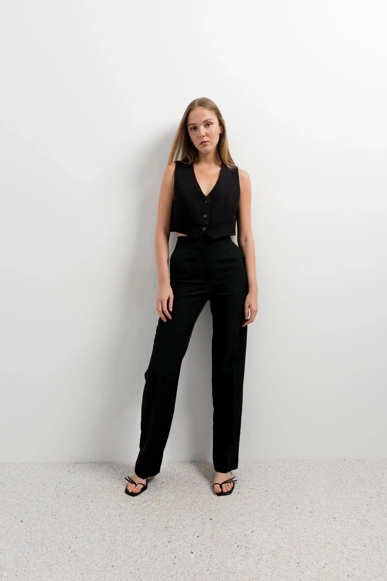 Femme portant un gilet court noir et une touche tendance avec pantalon et sandales ouvertes