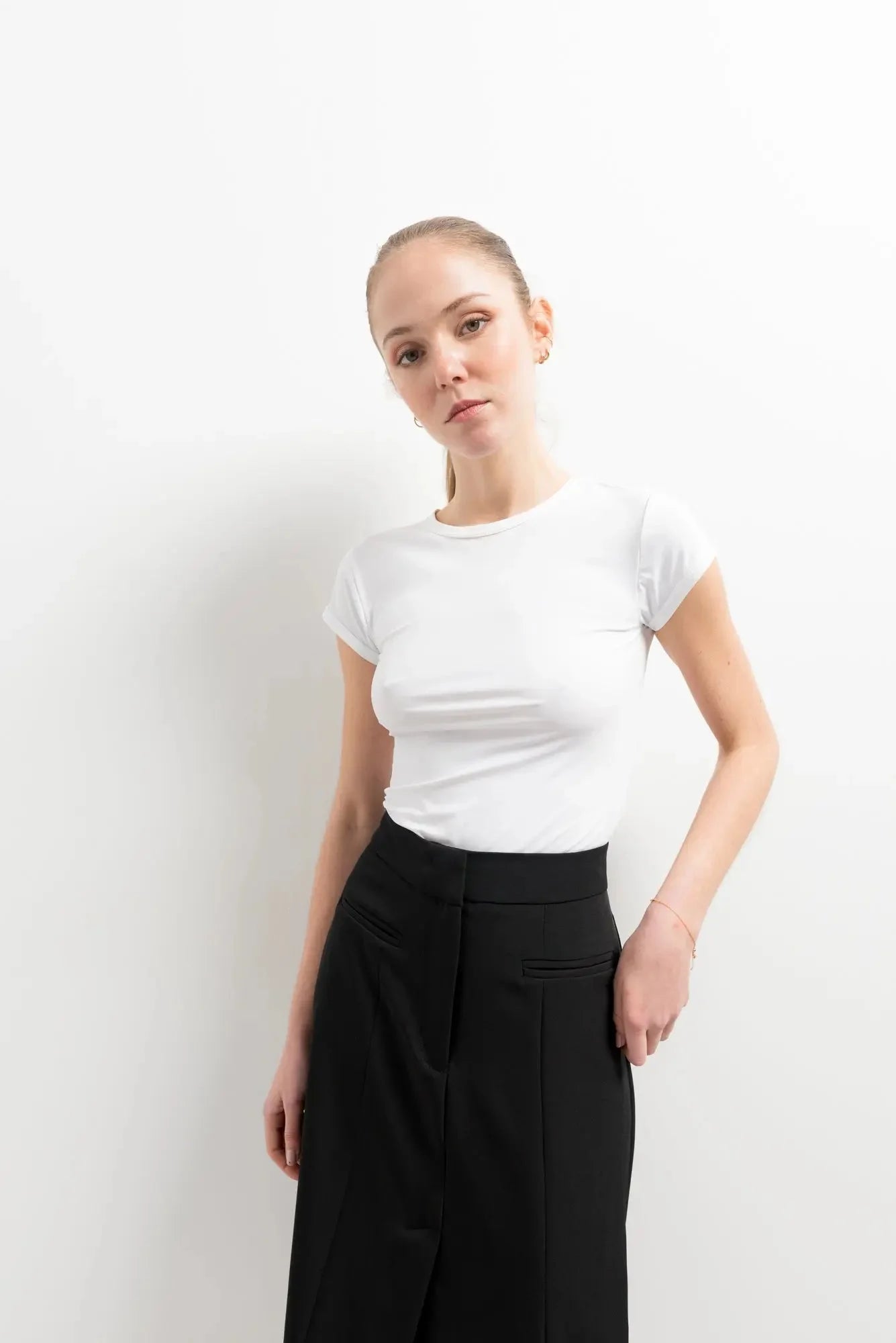 Femme présentant une jupe noire fendue avec un t-shirt blanc, capturant la tendance moderne avec simplicité.