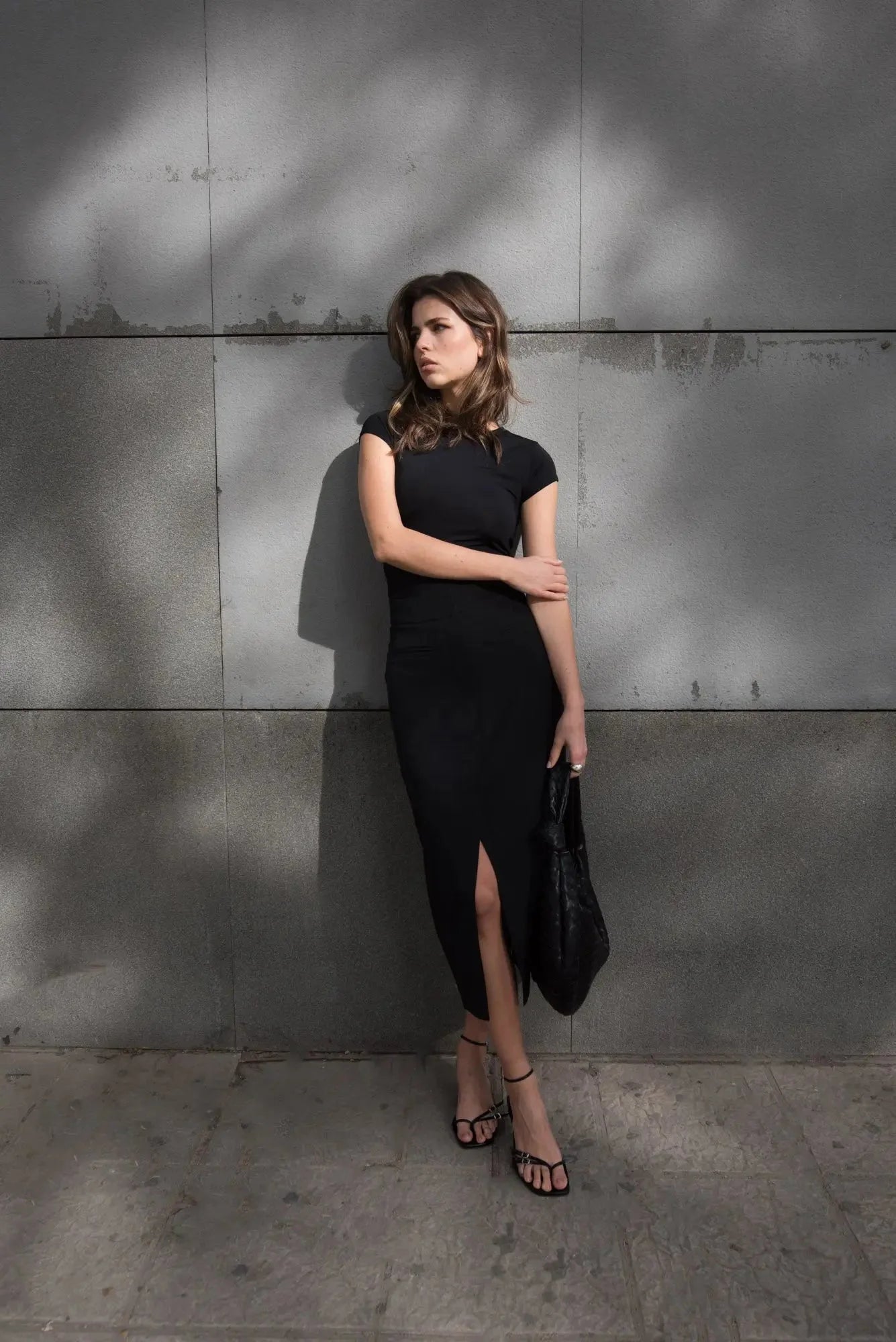 Femme posant avec une jupe noire fendue, exhalant un style chic et tendance dans un environnement contemporain.