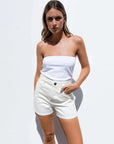 Modèle portant un ensemble haut blanc cassé et short beige taille haute, idéal pour l'été, mettant en avant le short en jean femme.