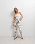 Femme modele debout en haut bandeau, mettant en valeur un pantalon motif femme à pois noir et blanc, sur un fond minimaliste.