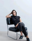 Femme élégante dans un ensemble style tunique et pantalon large en tricot, mettant en avant un haut sans manche femme, posant avec confiance sur une chaise noire.