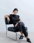 Modèle portant un ensemble style tunique et pantalon large en tricot, avec un haut sans manche femme, assis sur une chaise noire, affichant une allure chic et décontractée.
