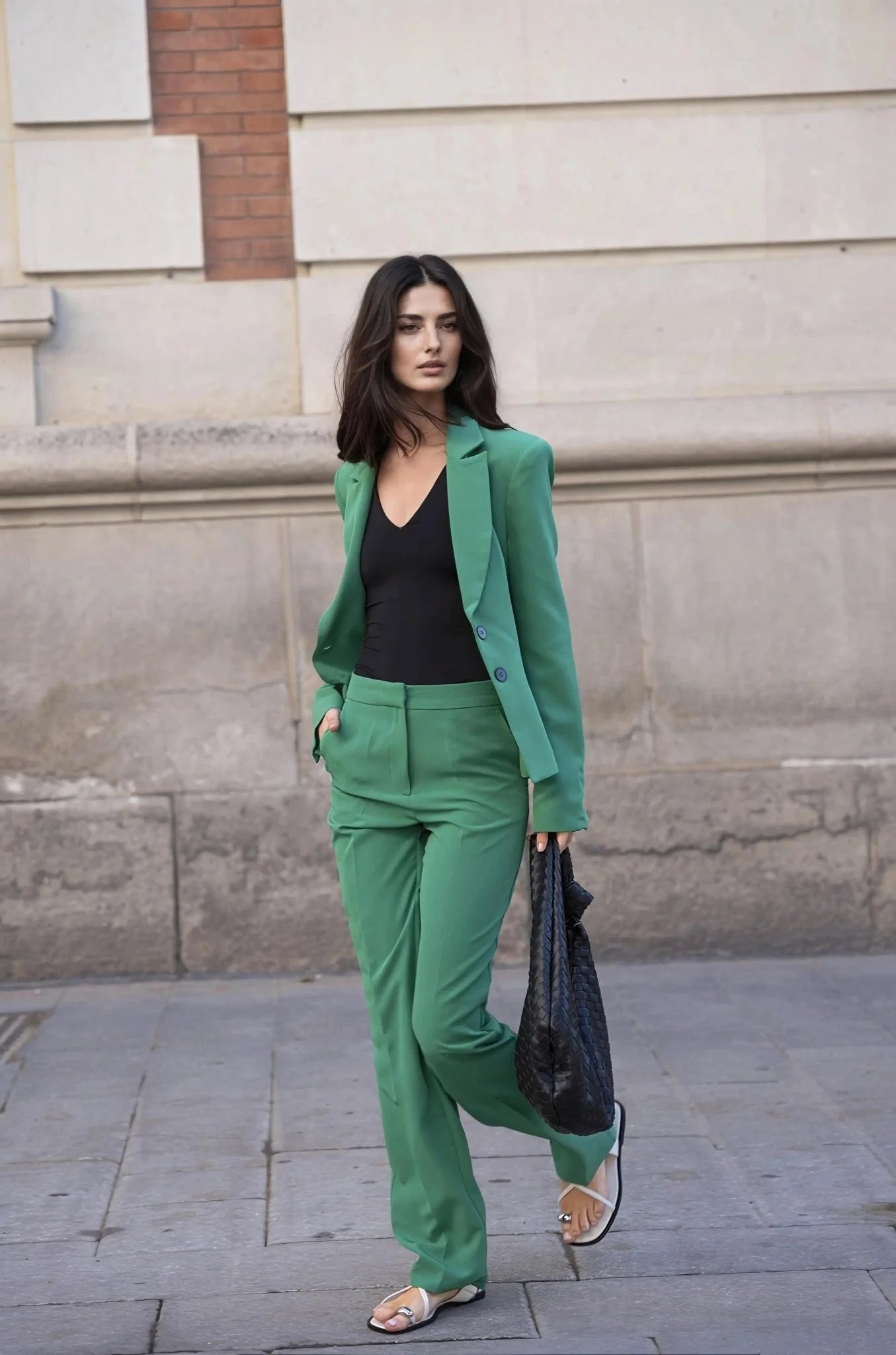 Femme en ensemble tailleur pantalon vert, haut noir, sandales blanches, sac noir