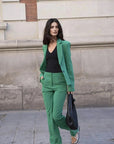 Femme professionnelle portant un ensemble tailleur pantalon vert femme, posant avec assurance devant un fond neutre.