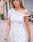 Femme portant un body asymétrique chic avec des manches longues drapées, en blanc, sur un fond urbain. Idéal pour toutes les occasions, ce Body asymétrique blanc est à la fois élégant et confortable.