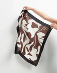 Foulard femme carré imprimé floral marron et blanc cassé tenu à la main, mettant en valeur le design élégant de cet accessoire.