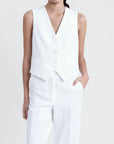 Femme en gilet blanc sans manches chic, coupe tailleur, avec pantalon blanc, affichant un look moderne et sophistiqué.