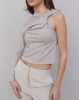 Haut asymétrique femme beige clair à une épaule, présenté de près avec une pose qui souligne le confort et l'élégance.