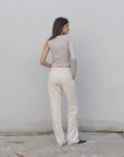 Vue arrière du haut asymétrique femme beige clair à une épaule, associé à un pantalon blanc pour un style chic.