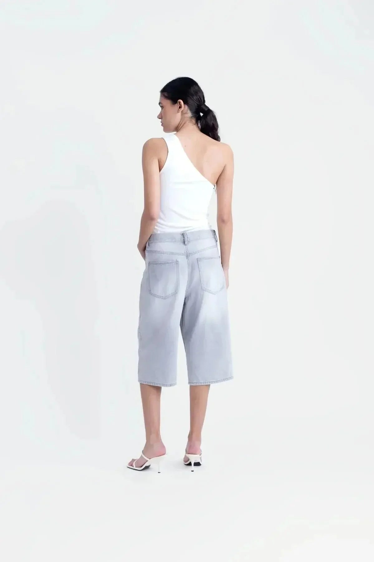 Vue arrière d'un haut asymétrique blanc, soulignant le design tendance et la polyvalence du vêtement.