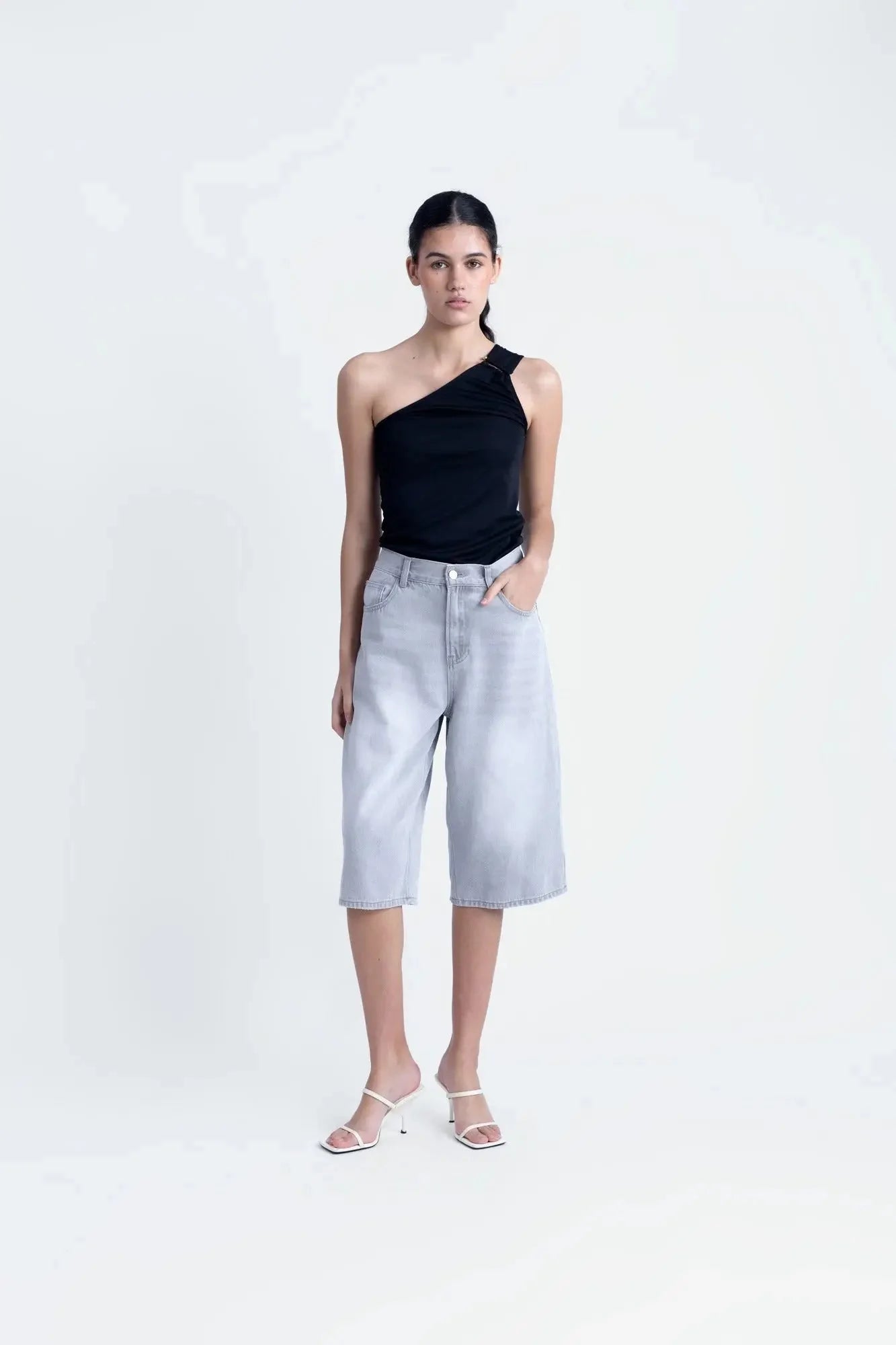 Modèle dans un haut asymétrique noir, mettant en valeur une tenue style décontracté avec une touche d'élégance.