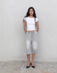 Femme posant avec style en bermuda jean femme gris clair, oversize et à taille haute, associé à un t-shirt blanc, parfait pour un look décontracté.