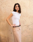 Femme posant en jupe cargo femme beige avec un haut blanc, avec un mur texturé en arrière-plan.