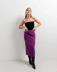 Femme stylée en jupe longue violette et top noir, montrant la polyvalence de ce vêtement élégant pour différentes occasions.