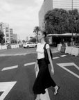 Femme marchant dans la rue en portant une jupe avec ceinture, captured in noir et blanc, mettant en avant la jupe midi pour un style urbain.