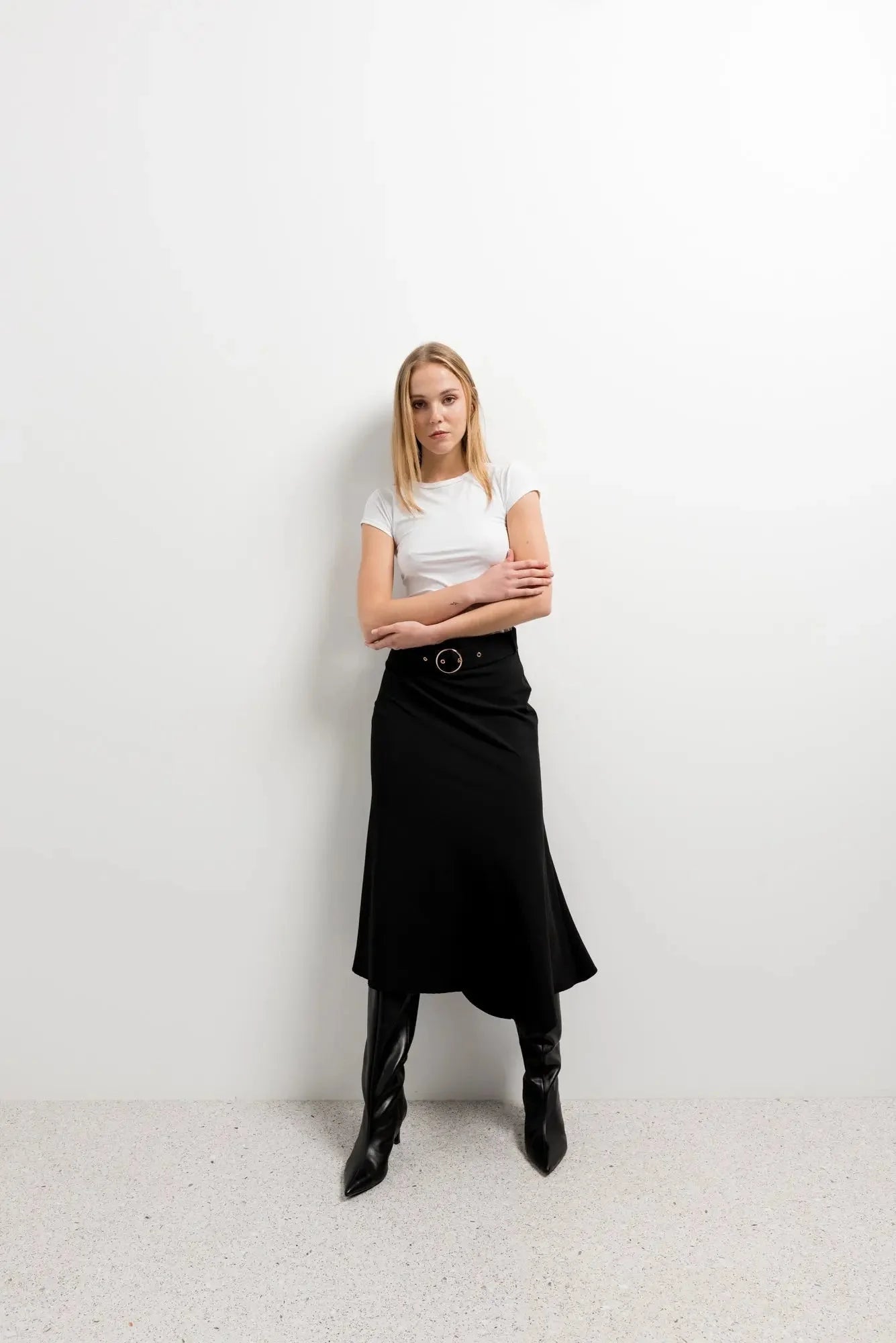 Femme portant une jupe midi noire avec ceinture, t-shirt blanc et bottes hautes