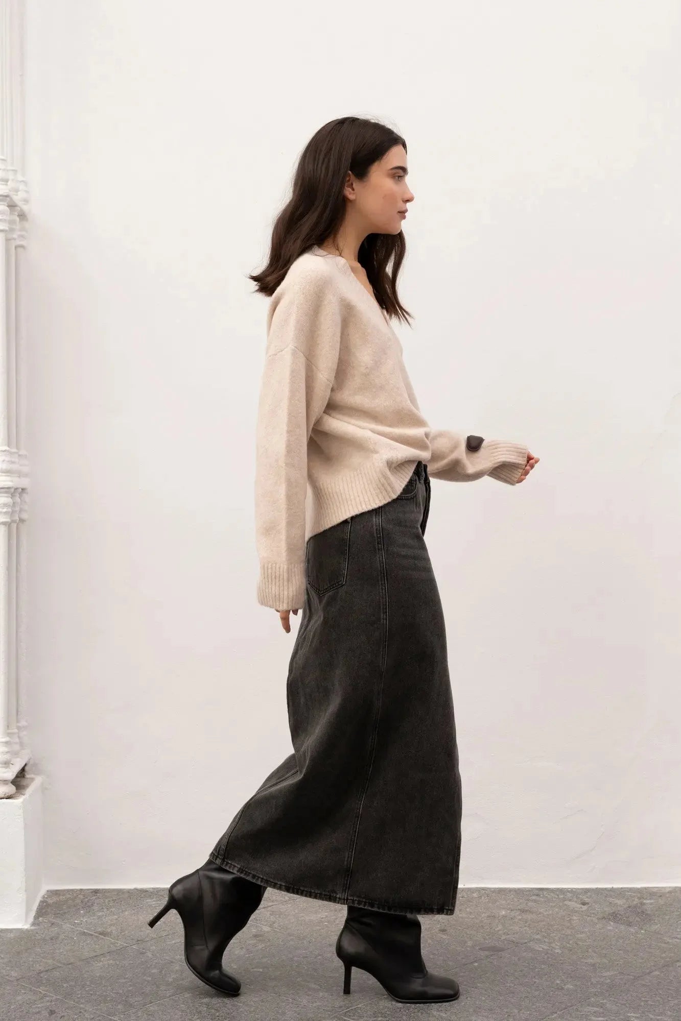 Femme portant une jupe midi polyvalente en denim avec fente, sweater beige et bottines noires