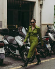 Femme portant une jupe verte satin longue avec une fente latérale, élégante pour un style polyvalent, se promenant parmi des motos.
