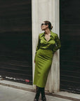 Modèle affichant une jupe verte satin longue et élégante, accentuant son apparence tout en se tenant contre un mur.