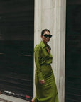 Femme marchant dans une jupe verte satin longue et chic, avec une fente latérale, offrant un look polychrome moderne, parfait pour diverses occasions.