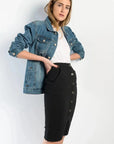Femme avec une jupe bouton devant noire en denim, posant avec une veste en jean, soulignant l'attrait polyvalent et durable de la jupe.