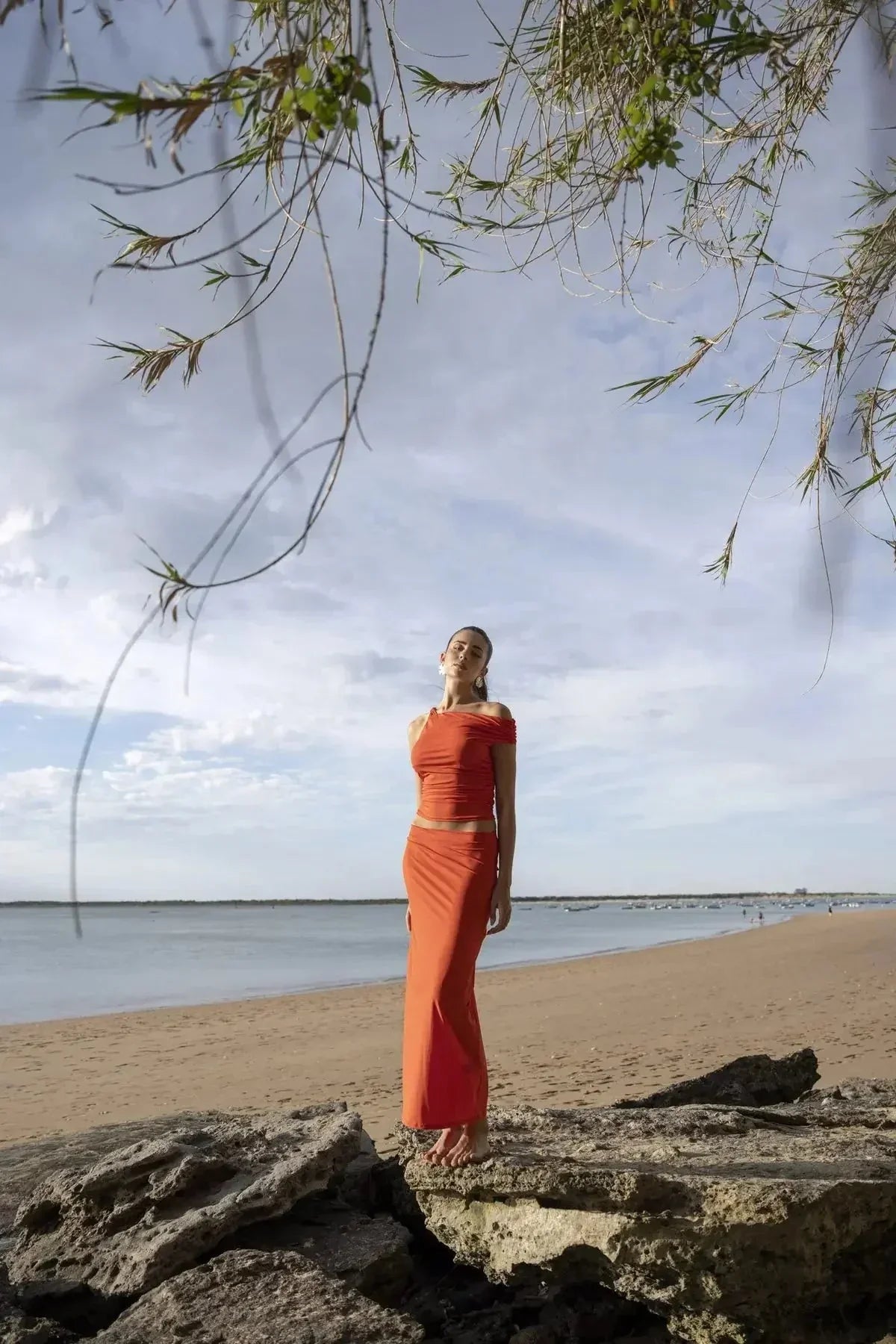 Femme dans une jupe rouge longue moulante taille basse en polyamide sur la plage, montrant un look sensuel avec une fente élégante.