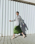 Femme marchant avec confiance en jupe verte satin et chemise à rayures, montrant l'élégance du style.