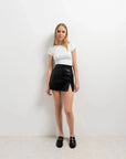 Modèle portant une jupe short simili cuir noir fendue, avec un t-shirt blanc, mettant en avant un style décontracté et élégant.