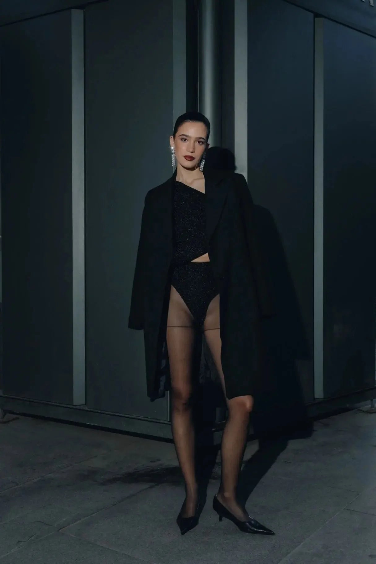 Femme portant un manteau ajusté en laine, bodysuit noir, hosiery, et talons pointus