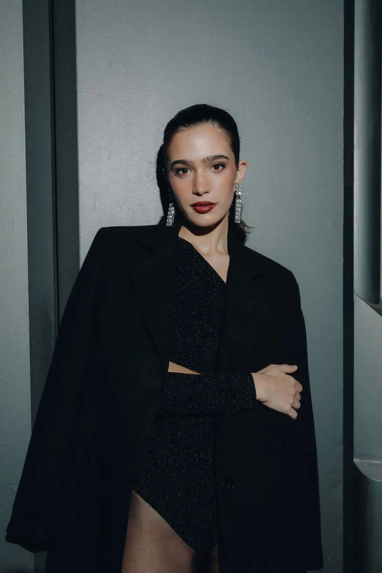 Femme portant un manteau ajusté en laine avec cape noire et boucles d’oreilles statement