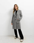 Manteau ajusté en laine pour femme, coloris gris, porté avec un pantalon noir pour un look moderne. Manteau femme chic hiver.