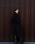 Femme montrant un manteau long chaud femme noir à double boutonnage de dos, avec un style moderne et élégant.