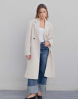 Femme montrant le manteau croisé femme beige clair, parfait pour un look décontracté et stylé, associé à un t-shirt blanc.