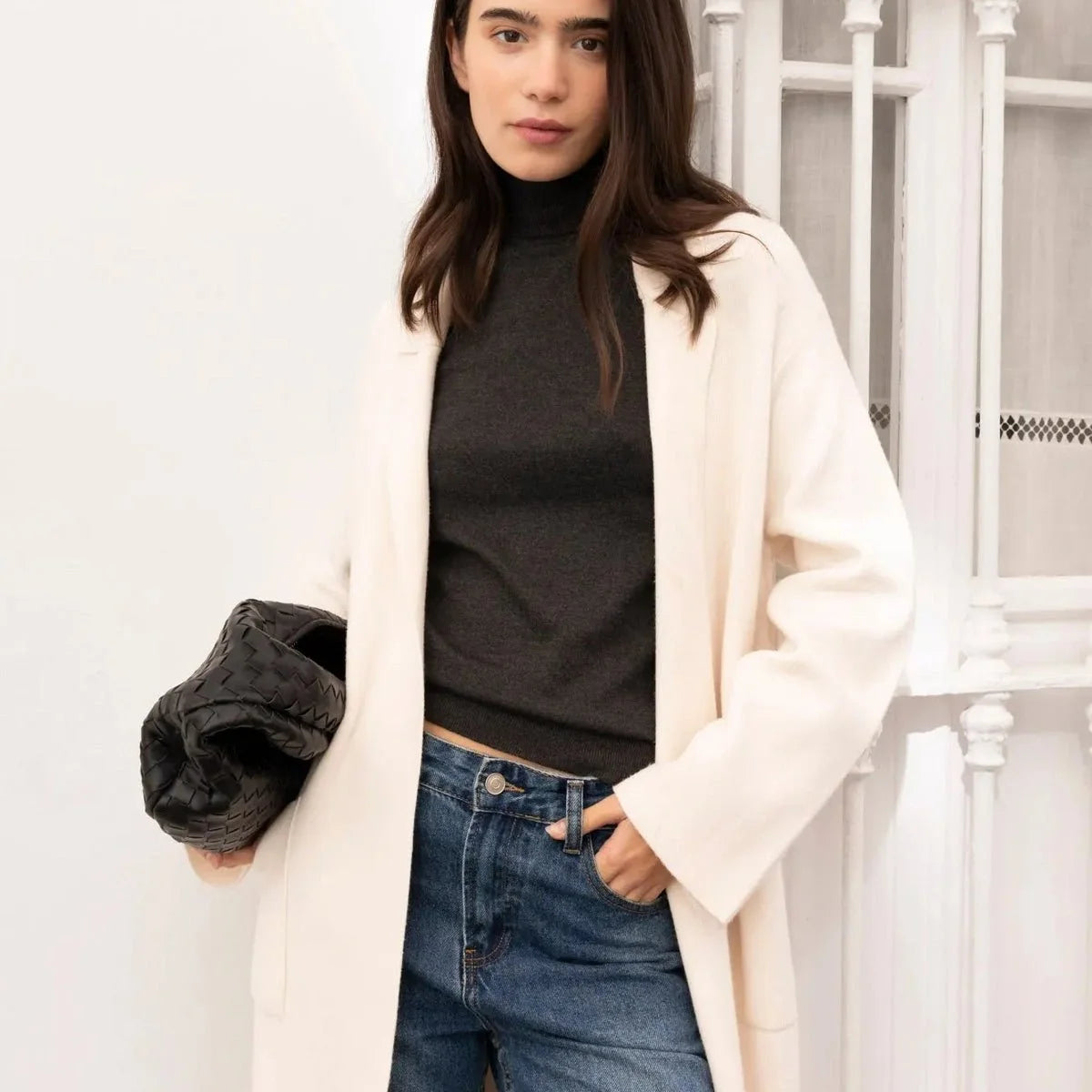 Femme posant en cardigan maille oversize cosy chic, avec un manteau en drap de laine et jean, style tendance pour l'automne.