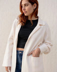 Femme portant un cardigan maille oversize cosy chic, avec un manteau en drap de laine, associé à un crop top noir et jean. Idéal pour un look élégant.