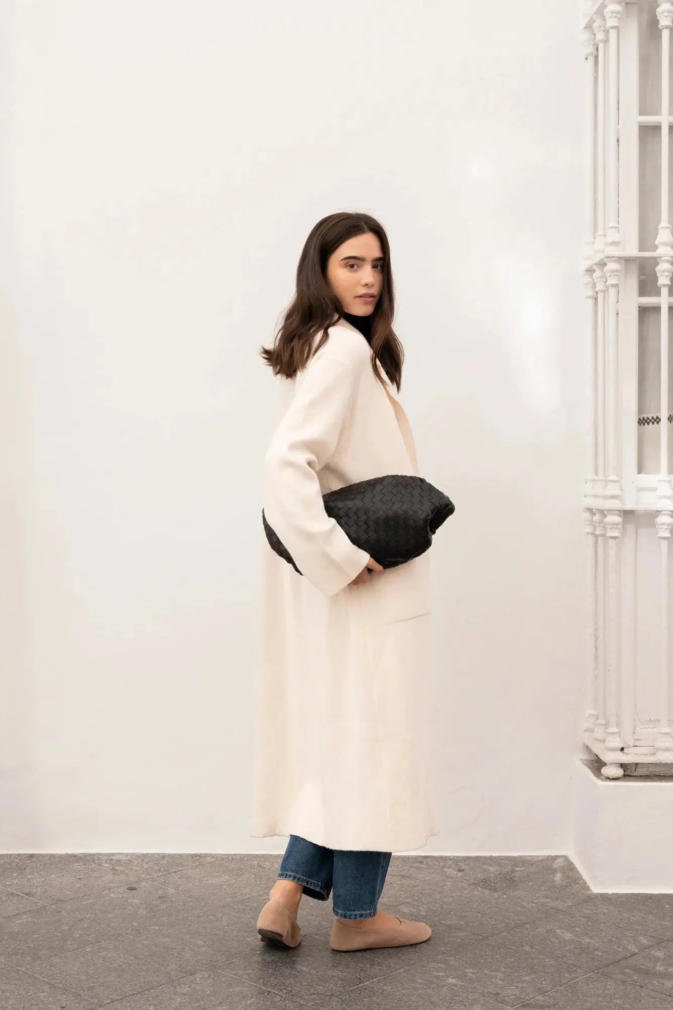Femme regardant sur le côté, portant un cardigan maille oversize cosy chic avec manteau en drap de laine et jean, look casual et élégant.