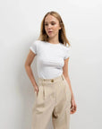 Femme posant en t-shirt blanc avec un pantalon court plissé taille basse beige, mettant en avant la versatile élégance du pantalon court noir femme.