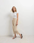 Femme stylée en t-shirt blanc et pantalon court plissé taille basse beige, illustrant un look décontracté élégant avec le pantalon court noir femme en tête.