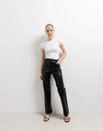 Femme posant avec assurance dans le Pantalon Effet Cuir Noir Élégant, associé à un top blanc. Idéal pour toutes celles qui recherchent un pantalon imitation cuir femme.