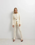 Femme habillée avec un pantalon habillé femme écru lumineux et blazer, style élégant, se tenant debout dans un environnement minimaliste.