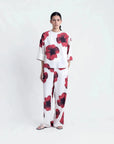 Modèle debout en toute confiance dans un pantalon habillé fluide – Coupe droite moderne – Blanc à fleurs rouges – Matière légère, mettant en avant le pantalon motif femme.