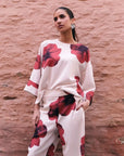 Femme posant avec élégance dans un pantalon habillé fluide – Coupe droite moderne – Blanc à fleurs rouges – Matière légère, mettant en avant le pantalon motif femme.