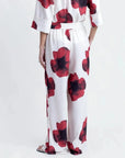 Vue arrière d'une femme dans un pantalon habillé fluide – Coupe droite moderne – Blanc à fleurs rouges – Matière légère, révélant le pantalon motif femme.