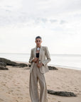 Portrait d'une femme en pantalon large et fluide femme beige sur la plage, tenant un blazer et affichant une allure moderne.