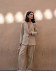 Femme portant un costume beige, associe un pantalon large et fluide femme avec un blazer chic dans un cadre minimaliste.